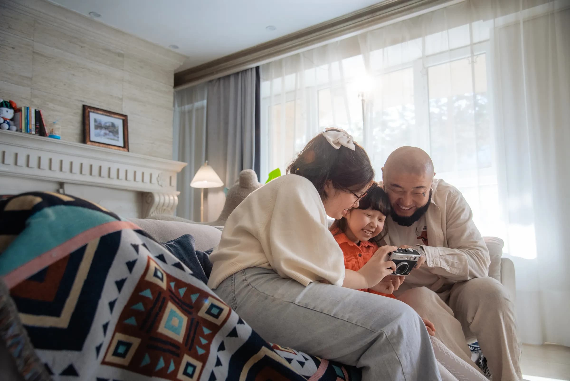 Parents and daughter laughing together with a camera in a sunlit living room